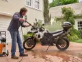 Uomo lava moto a idropulitrice in giardino. Ecco come lavare la moto a casa per mantenerla splendente.