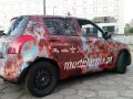 Samochód z okleiną imitującą rdzę, z napisem "modelarnia.pl" i ikonami modeli. Reklama na samochodzie zarobek.