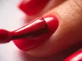 Application d'un vernis rouge vif sur un ongle. Le temps de séchage du vernis à ongles est crucial pour un fini parfait.