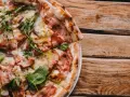 Pyszna pizza carbonara z chrupiącym boczkiem i rukolą na drewnianym stole.