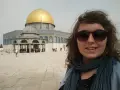 Uśmiechnięta kobieta w okularach przeciwsłonecznych robi selfie na tle Kopuły na Skale. Wokół widać turystów, co sugeruje, że w Jerozolimie jest bezpiecznie.