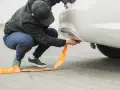 Mężczyzna mocuje pomarańczową linę holowniczą do samochodu. Pamiętaj o ograniczeniach prędkości podczas holowania, by zapewnić bezpieczeństwo.