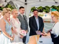 Ceremonia ślubna nad jeziorem, panna młoda w białej sukni, pan młody w garniturze, urzędniczka w przyłbicy.