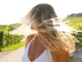 Wiatr rozwiewa blond włosy kobiety, odsłaniając jej profil. To naturalny sposób na siwe włosy bez farbowania, podkreślający piękno w każdym wieku.