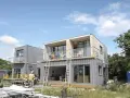 Maison en container prix : construction moderne à deux étages avec balcons, fenêtres panoramiques et un ouvrier en gilet de sécurité.