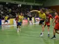 Gracz w żółtej koszulce rzuca piłkę ręczną podczas meczu. W tle kibice i zawodnicy w czerwonych strojach. Stal Gorzów walczy o zwycięstwo.