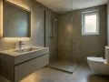 Salle de bain moderne avec lavabo en béton ciré, douche à l'italienne et WC suspendu. L'éclairage indirect du miroir crée une ambiance douce.