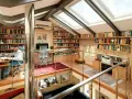 Un uomo lavora in una luminosa libreria mansarda, circondato da scaffali pieni di libri e illuminato da lucernari.