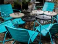 Teal metal chairs and tables, perfect for outdoor use, sit empty on a wet patio.