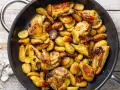 Pollo con patate in padella, dorato e saporito, con erbe aromatiche. Un piatto rustico e invitante.