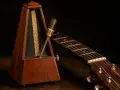 Un métronome en bois et une guitare acoustique, prêts pour la répétition. Le métronome bat la mesure, le temps de **half time** est en cours.