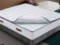 Un matelas king size mémoire de forme, blanc matelassé, sur un sommier gris. Confort garanti pour des nuits paisibles.