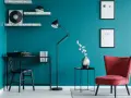 Bureau noir avec machine à écrire, lampe sur pied, fauteuil rouge et étagères sur un mur bleu ou vert canard.