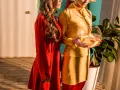 Dwie kobiety w stylizacjach inspirowanych **modą lat 60.**, jedna w czerwonej sukience, druga w żółtym kostiumie, trzymająca kulę z rybkami.