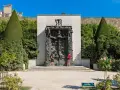 La Porte de l'Enfer, une œuvre monumentale de Rodin, se dresse majestueusement, encadrée par des arbres taillés et un mur de pierre. Deux visiteurs contemplent cette sculpture complexe.