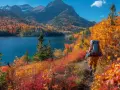 Un randonneur explore un sentier bordé d'arbustes aux couleurs flamboyantes, idéal pour randonner en octobre en France, avec un lac bleu et des montagnes en arrière-plan.