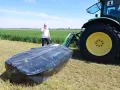 Mężczyzna prezentuje nowoczesne kosiarki dyskowe SaMASZ obok zielonego traktora na polu.
