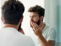 Hombre con barba regia se mira al espejo, acariciando su rostro.