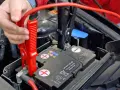 Hand befestigt rote Klemme an Autobatterie. Die richtige **Starthilfe Reihenfolge** ist entscheidend für die Sicherheit.