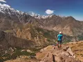 Widok na ośnieżone szczyty górskie Jebel Toubkal. Turystka podziwia panoramę z skalistego zbocza.