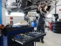 Warsztat samochodowy: mechanik pracuje pod podniesionym autem, wózek z narzędziami na pierwszym planie.
