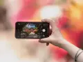 Une main tient un smartphone pour capturer un escalier fleuri menant à un pavillon. L'écran montre les bases de la photographie, avec des options comme "PHOTO" et "PORTRAIT".