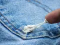 Ein Finger versucht, Kaugummi von Jeans zu entfernen. Der klebrige Kaugummi zieht sich zäh.