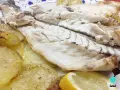 Lubina al horno jugosa y tierna, acompañada de patatas asadas y rodajas de limón fresco.