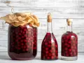Ein großes Glas und zwei Flaschen gefüllt mit Kirschen und Alkohol. Perfekt für ein schnaps selber machen rezept.