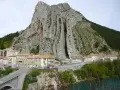 Imponerande klippformation vid Route Napoléon. En by klättrar uppför bergssluttningen, med en bro och en turkos flod nedanför.