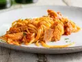 Spaghetti al tonno conditi con un sugo saporito e ricchi pezzi di tonno, guarniti con prezzemolo fresco.