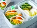 Leckeres Fingerfood für Kinder: Wraps mit Gemüse und Käse, garniert mit kleinen Dino-Spießen. Dazu Gurken und Apfelschnitze.