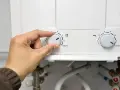 Mano girando el dial del termo eléctrico para cerrar la llave de paso.