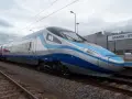 Nowoczesny pociąg Pendolino w kolorach biało-niebieskim stoi na torach przy peronie.