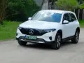 Biały Mercedes EQB na drodze gruntowej, otoczony zielenią.