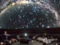 Besucher im Planetarium Berlin liegen und sitzen und blicken gebannt auf die Projektion der Milchstraße und funkelnder Sterne.