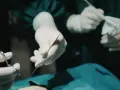 Dłonie chirurga w rękawiczkach trzymające narzędzia chirurgiczne i gazę.