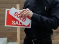 Hombre coloca cartel de "Vendido" sobre uno de "En Venta". Una venta rápida, quizás por debajo del valor de referencia.