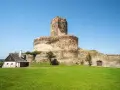 Zamek Bolków, potężna warownia z kamienia, góruje nad zielonym wzgórzem. Obok stoi niewielki domek.