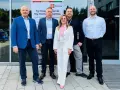 Pięć osób w eleganckich strojach stoi przed budynkiem z banerem "m Finanse".
