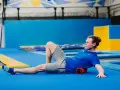 Mężczyzna ćwiczy z wałkiem do masażu na niebieskiej macie gimnastycznej.
