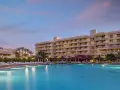 Basen i hotel o zachodzie słońca. Wiele leżaków i palm. Idealne miejsce na wakacje, zgodnie z licznymi sindbad club opinie.