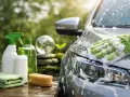 Tvätta bilen hemma med miljövänliga produkter. En hand med tvätthandske tvättar bilen i solljus.