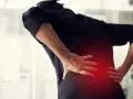 Osoba w czarnej bluzce trzyma się za plecy, gdzie widać czerwony obszar bólu.