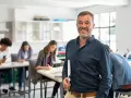 Professore sorridente in aula con studenti. La sua laurea per insegnare alle superiori è evidente dalla sua sicurezza.
