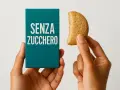 Mani che tengono una scatola con scritto "SENZA ZUCCHERO" e un biscotto senza zucchero.