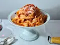 Breite Bandnudeln mit herzhaftem bolognese ragu, bestreut mit Parmesan. Daneben ein Glas Rotwein und Besteck.