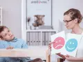 Bambino con autismo durante un test, mentre un terapista mostra faccine felici e tristi.