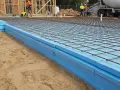 Układanie płyt XPS na fundamentach pod wylewkę betonową. Widoczna siatka zbrojeniowa.