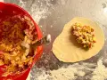 Fyllning till piroger recept läggs på deg. En röd skål med fyllning syns till vänster.